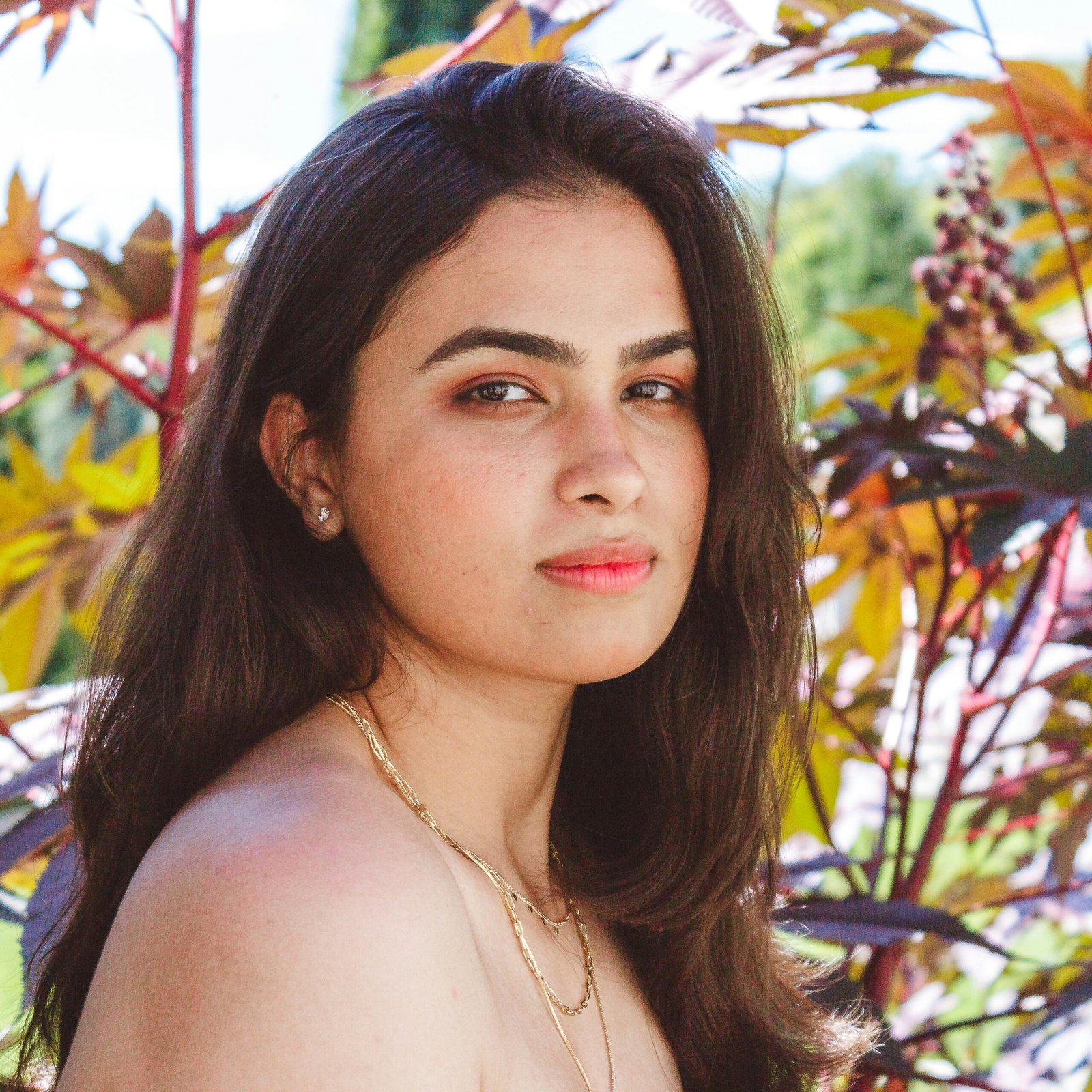 Portrait of a woman with long hair posing outdoors with foliage in the background.