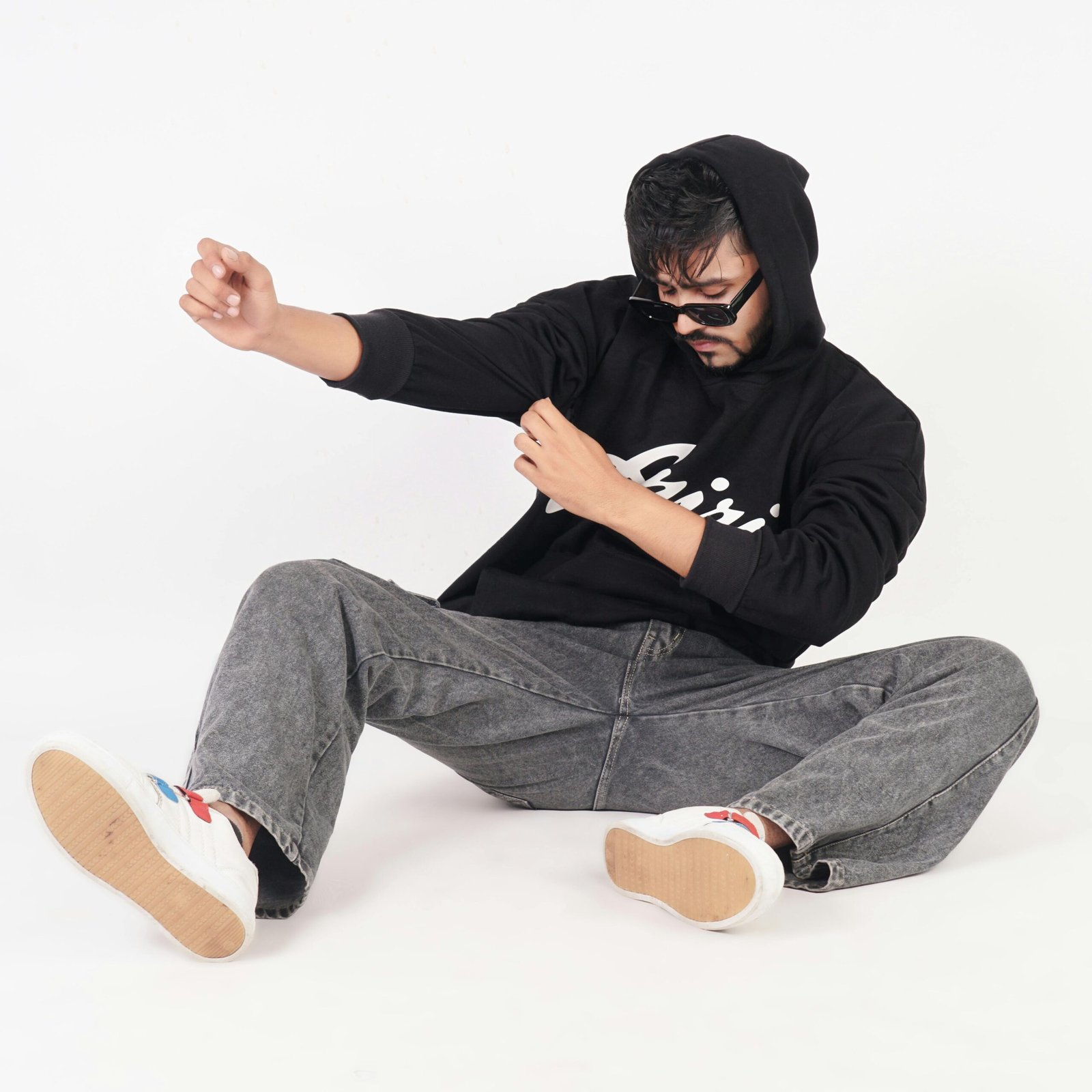 Urban photo shoot of a stylish model in black hoodie and jeans striking a relaxed pose.