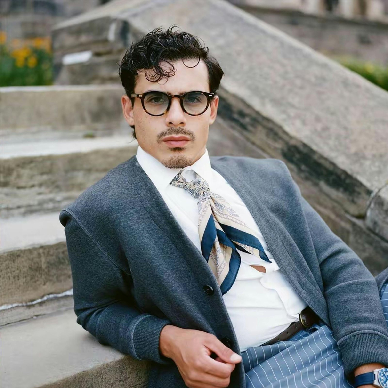 Casually dressed man with glasses lounging on stone steps outdoors.